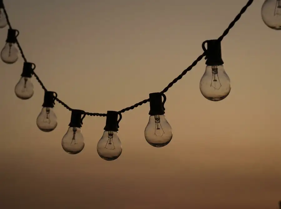 A single strand of clear glass bulbs on a dark cord, lit and hanging in a curve against open evening sky, with nothing else in the frame.